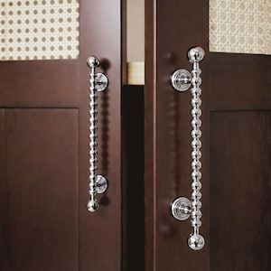 May include: Two dark brown wooden cabinet doors with decorative silver handles. The handles are made of small, round, silver beads strung together. The cabinet doors have a woven pattern in the upper section. The doors are for a cabinet.