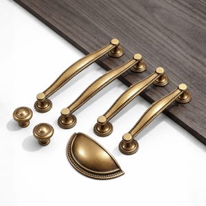 May include: A set of antique brass cabinet hardware, including four pull handles, two knobs, and a cup pull. The hardware features a detailed design with a warm, aged finish, perfect for adding a vintage touch to furniture or cabinetry.