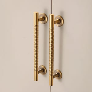 May include: Two brass cabinet pulls with a honeycomb pattern on a light gray cabinet. The pulls are cylindrical with a circular base and top. The hardware is a warm gold color.
