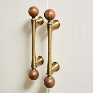 May include: Two brass door pulls with a wooden ball at each end. The pulls have a long, slender design with a flared base and a curved handle. The wooden balls are a warm brown color, and the brass has a polished finish.