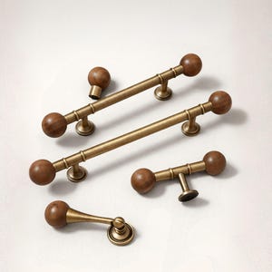 May include: A collection of cabinet hardware featuring a warm brass finish and wooden accents. The set includes various sizes of pulls and knobs, with a classic, timeless design. The wooden spheres add a touch of natural elegance to the hardware.