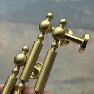 May include: Close-up of several brass-colored cabinet pulls. Each pull features a cylindrical body with decorative ball accents and a circular mounting plate. The hardware has a matte finish and a classic design.