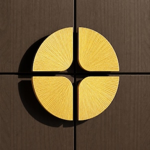 May include: Close-up of a dark brown wooden cabinet door with four gold-colored, semi-circular handles. Each handle has a textured, sunburst design, creating a symmetrical, decorative pattern. The handles are mounted on the cabinet doors.