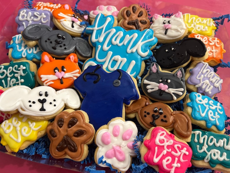 May include: Assortment of decorated sugar cookies in various shapes and colors, including paw prints, animals, and messages like "Thank You" and "Best Vet".