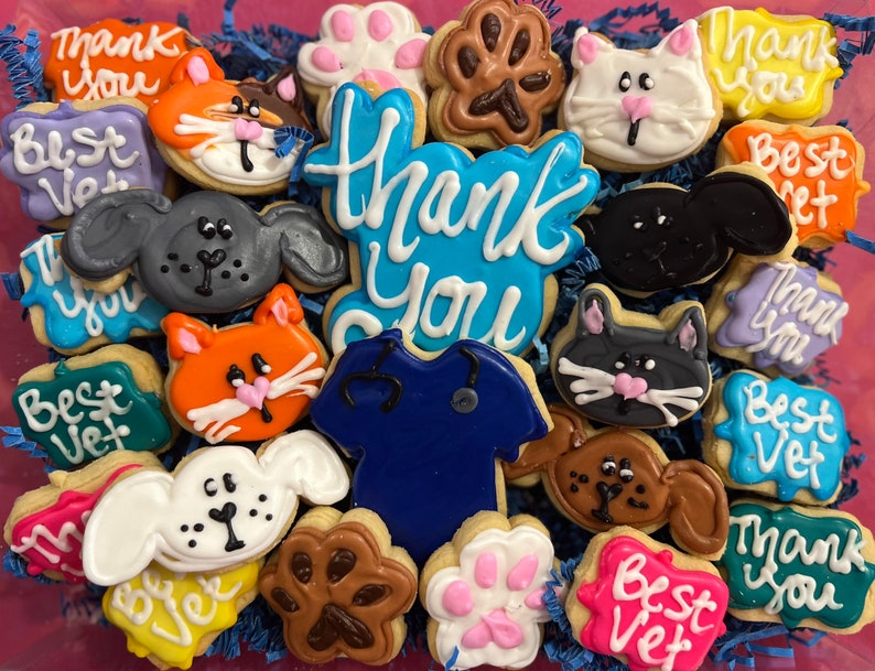 May include: Assortment of decorated sugar cookies with various animal and paw print designs. The cookies are decorated with blue, pink, green, yellow, white, and brown icing. The cookies have text that reads "Thank You", "Best Vet", and "Best Vet".
