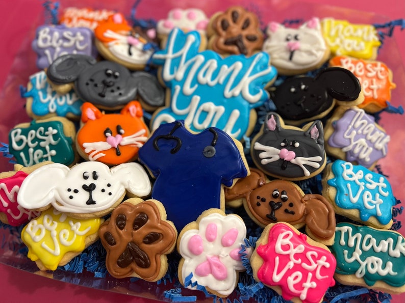 May include: A collection of decorated sugar cookies with various designs, including paw prints, animals, and the words "Thank You" and "Best Vet".