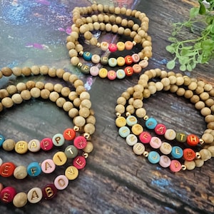 May include: Three wooden beaded bracelets with colorful letter beads spelling out the words "Have Faith", "Rise Above", and "Be Happy".