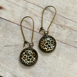 May include: A pair of gold tone dangle earrings with round glass cabochons featuring a leopard print design.