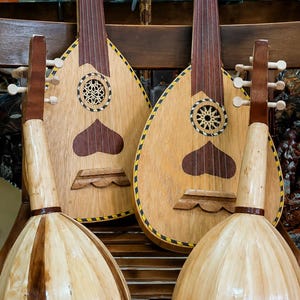 Peut inclure: Quatre ouds en bois avec des corps brun clair et des manches brun foncé sont exposés sur un banc en bois. Les ouds présentent des motifs complexes et des accents en forme de cœur, mettant en valeur l'artisanat traditionnel.