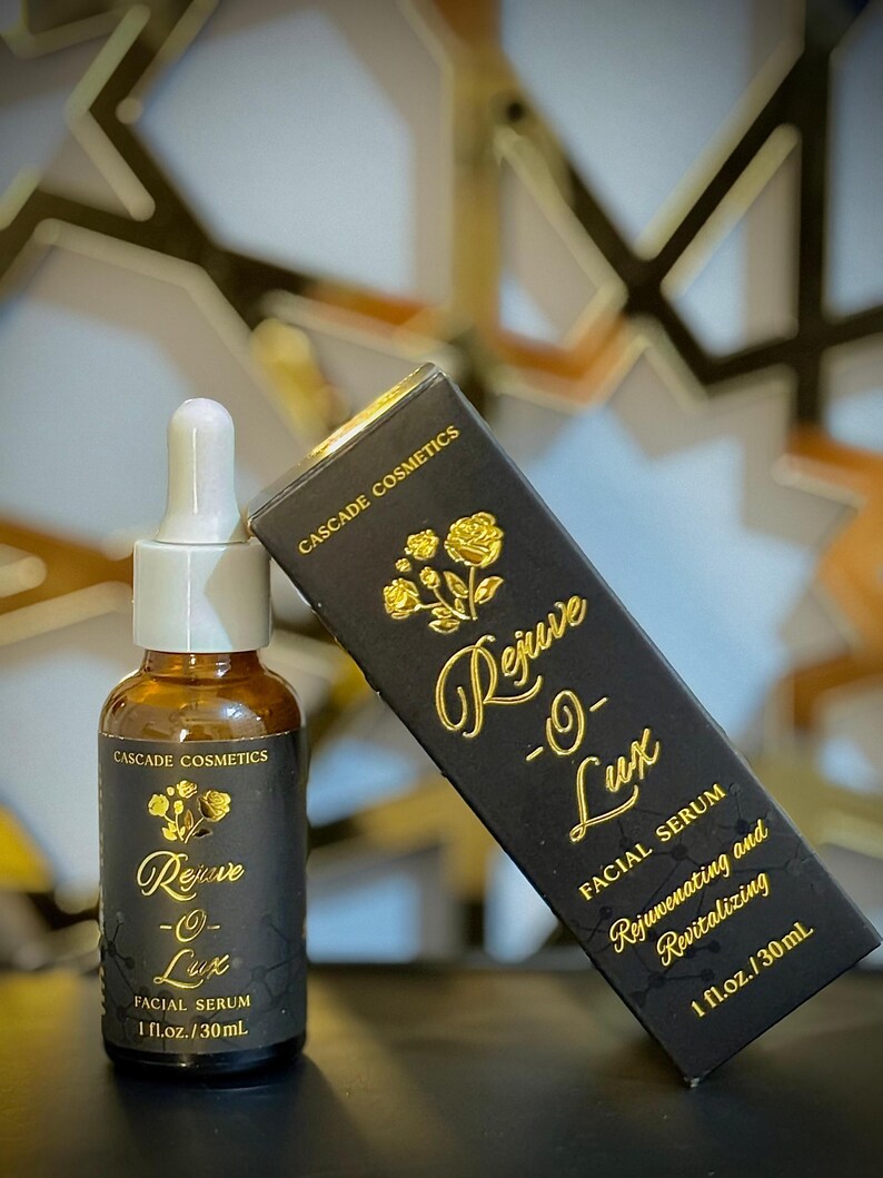 May include: A brown glass bottle with a white dropper and a black label with gold text that reads "Rejuve -O- Lux FACIAL SERUM 1 fl.oz./30mL". A black box with gold text reads "CASCADE COSMETICS Rejuve -O- Lux FACIAL SERUM Rejuvenating and Revitalizing 1 fl.oz./30mL".