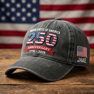 May include: A gray baseball cap with the text "UNITED STATES OF AMERICA" and "250 ANNIVERSARY 1776-2026" in red, white, and blue. The cap also features a small American flag and the name "JAKE".