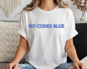 May include: White t-shirt featuring the blue text "NO CODES BLUE". The shirt has short sleeves and a casual fit. The model is wearing blue jeans.