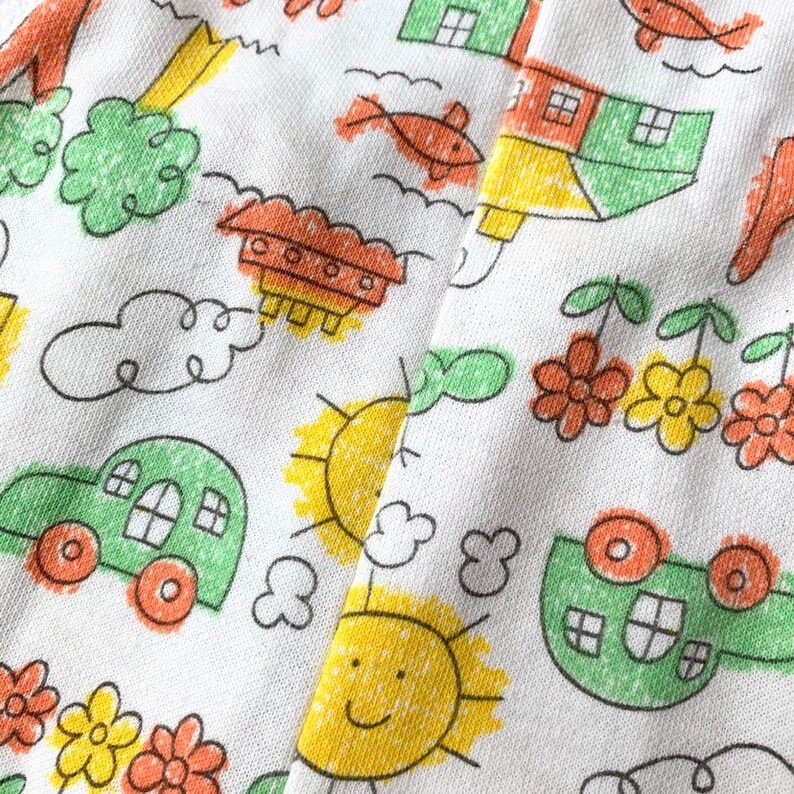 May include: White fabric with a repeating pattern of hand-drawn illustrations in yellow, orange, and green. The illustrations include houses, cars, suns, flowers, and clouds.