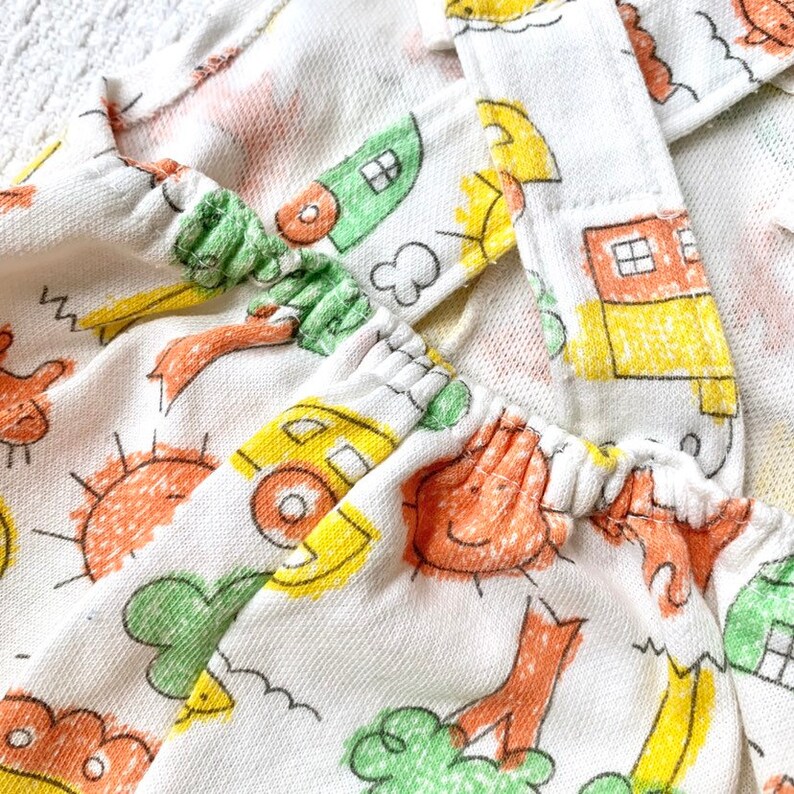 May include: White cotton fabric with a yellow, orange, and green print of houses, suns, and trees. The fabric has a gathered elastic band at the top.