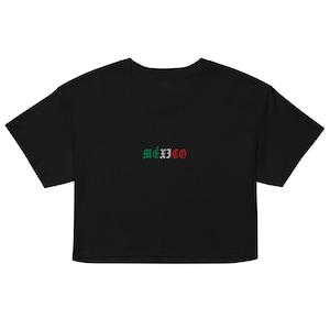 May include: A black cropped t-shirt featuring the word MÉXICO embroidered in the center of the chest. The letters are colored in green, white, and red, reflecting the colors of the Mexican flag, using a gothic-style font for the text.