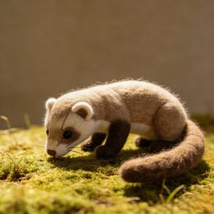 May include: A handcrafted ferret figurine with a light brown body, dark brown legs, and a long, bushy tail. The ferret has a white face with dark eyes and is posed on a bed of green moss. The figurine is made of soft, textured material.