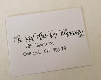 Puede incluir: Un sobre rectangular blanco con caligrafía negra escrita a mano. El texto dice: Mr. and Mrs. Tim Flannery, 789 Benny Dr., Oakland, CA 98179. La dirección está escrita en una combinación de estilos cursivo y de imprenta en la parte frontal.