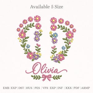 May include: Floral embroidery design featuring the name "Olivia" in pink script, surrounded by a floral wreath in pink, purple, yellow, and blue. The design includes a bow and foliage. Text at the top says "Available 5 Size".