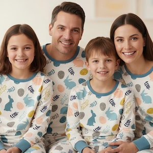 Puede incluir: Una familia de cuatro personas con pijamas a juego. Los pijamas son blancos con un estampado de conejitos azules, huevos y ramitas. Los pijamas tienen ribetes azules alrededor del cuello y las mu&ntilde;ecas. La familia sonr&iacute;e a la c&aacute;mara.