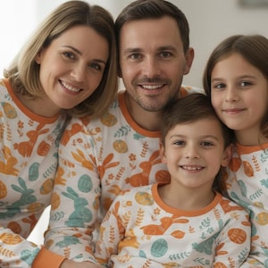 Puede incluir: Una familia de cuatro personas con pijamas a juego. Los pijamas son blancos con un estampado de conejitos y huevos de Pascua en naranja y turquesa. La familia sonr&iacute;e a la c&aacute;mara.