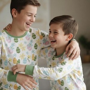 Pu&ograve; includere: Due persone indossano pigiami a maniche lunghe abbinati con un motivo a uova di Pasqua e floreale. I pigiami hanno finiture verdi sul colletto e sui polsini. Entrambe le persone sorridono e si abbracciano.