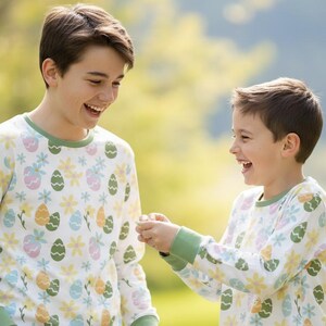 Pu&ograve; includere: Due persone indossano pigiami a maniche lunghe abbinati con un motivo di uova di Pasqua e fiori. I pigiami sono bianchi con finiture verdi e presentano uova e fiori dai colori pastello. Le persone sorridono e ridono all'aperto.