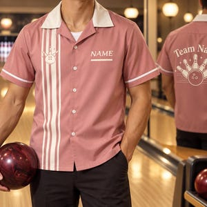 May include: A dusty rose short-sleeved bowling shirt with a white notched collar and white sleeve trim. The front features three vertical white stripes, a bowling ball and pin graphic, and the text NAME. The back displays a bowling graphic and Team Name.