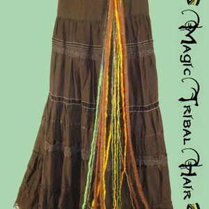 May include: A long, colorful strand of yarn hair extensions with a silver flower charm attached to the top. The extensions are hanging from a brown skirt with lace trim.