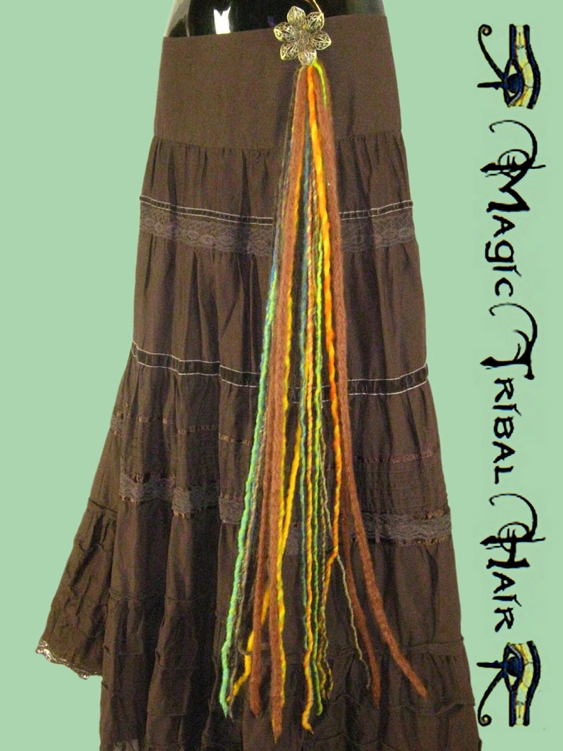 May include: A long, colorful strand of yarn hair extensions with a silver flower charm attached to the top. The extensions are hanging from a brown skirt with lace trim.