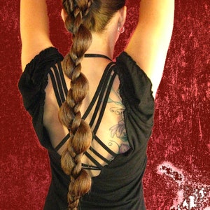 Op de afbeelding: Een vrouw met lang bruin haar dat in een gevlochten paardenstaart is gestyled. Ze draagt een zwart, mouwloos topje met een gekruiste rug.