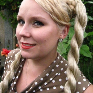 May include: A woman with blonde hair styled in a braided ponytail, wearing a brown and white polka dot dress. She is wearing a silver necklace and a small earring.