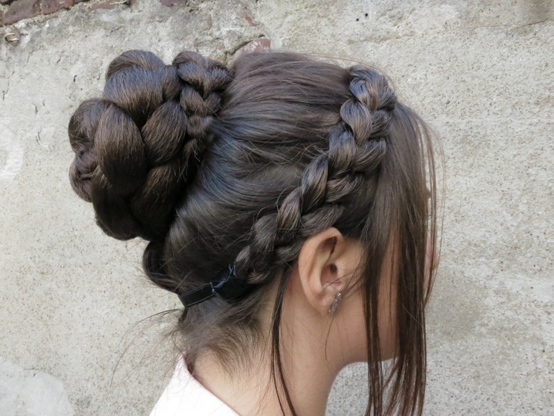 May include: A woman with long brown hair styled in a braided crown and a bun. The bun is secured with a black elastic band.