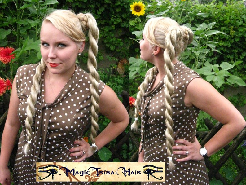 May include: A woman with blonde hair styled in two long, thick braids. She is wearing a brown and white polka dot dress. The dress has a V-neck and short sleeves. The woman is standing in a garden with green plants and flowers.