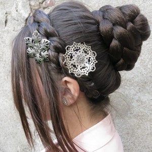 May include: A woman with long brown hair styled in a braided bun with two silver hair clips. One clip is a floral design and the other is a circular design.
