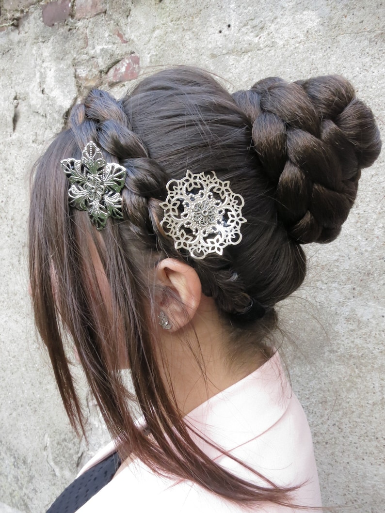 May include: A woman with long brown hair styled in a braided bun with two silver hair clips. One clip is a floral design and the other is a circular design.