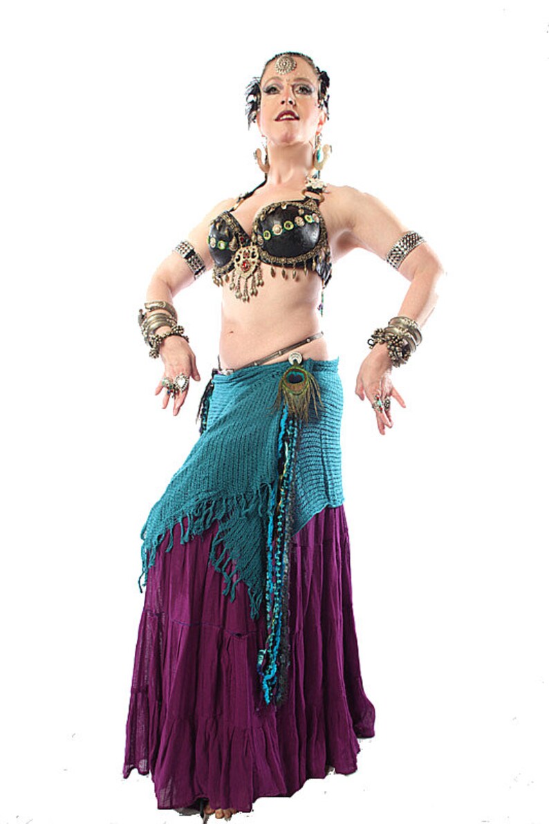 May include: A woman wearing a black and gold bra with a peacock feather accent, a turquoise and purple skirt, and multiple silver bracelets on both wrists.