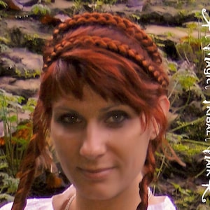 May include: A woman with long, red hair styled in a braided crown. The braids are woven into a thick, intricate pattern. She is wearing a white shirt and has a natural makeup look.