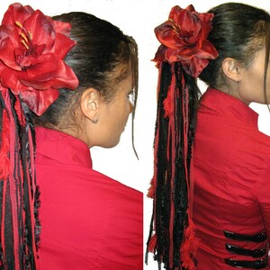 May include: A red fabric flower hair clip with black and red fabric strands hanging down. The flower is attached to a black elastic band.