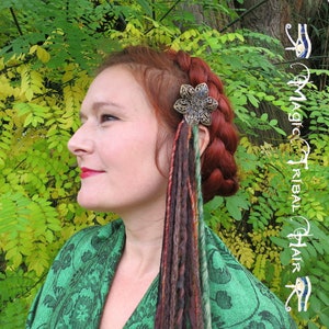 May include: A woman with red hair wearing a green shawl with a floral pattern. She has a silver and black flower hair clip with colorful dreadlocks hanging from it.