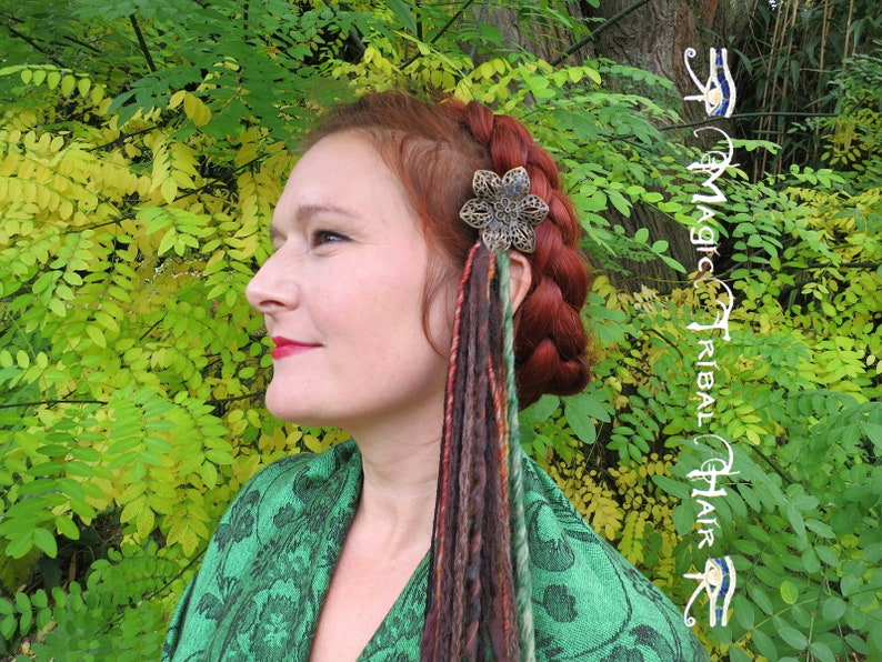 May include: A woman with red hair wearing a green shawl with a floral pattern. She has a silver and black flower hair clip with colorful dreadlocks hanging from it.