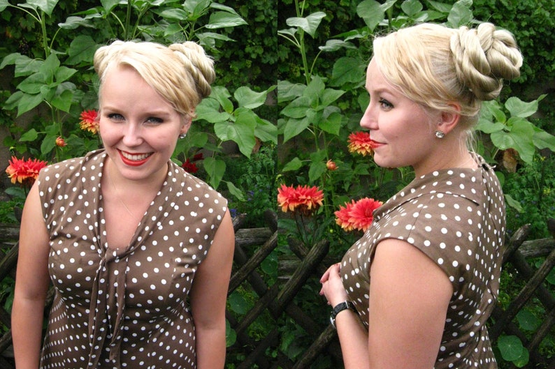 May include: Two women with blonde hair wearing brown and white polka dot dresses. The women are standing in front of a green leafy background.