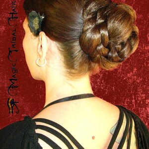 Op de afbeelding: Een vrouw met lang bruin haar dat in een gevlochten knot is gestyled. Ze draagt een zwart topje met bandjes die in de rug kruisen.