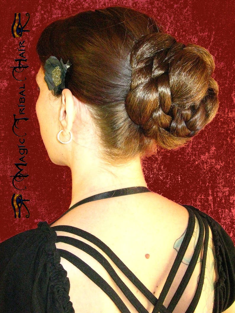 Op de afbeelding: Een vrouw met lang bruin haar dat in een gevlochten knot is gestyled. Ze draagt een zwart topje met bandjes die in de rug kruisen.