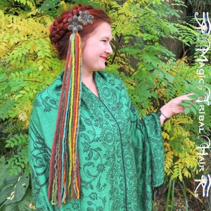 May include: A woman with a braid in her hair wears a green shawl with a floral pattern. She has a silver hair clip with a colorful yarn braid hanging from it.