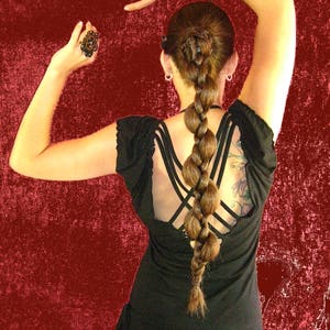 Op de afbeelding: Een vrouw met lang bruin haar dat in een gevlochten paardenstaart is gestyled, draagt een zwart, mouwloos topje met een kruisrugontwerp en een bruine rok.
