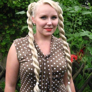 May include: A woman with blonde hair styled in two braids wears a brown dress with white polka dots. The dress has a bow at the neckline.