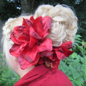 May include: A woman with blonde hair styled in a bun with a large red flower hair clip.