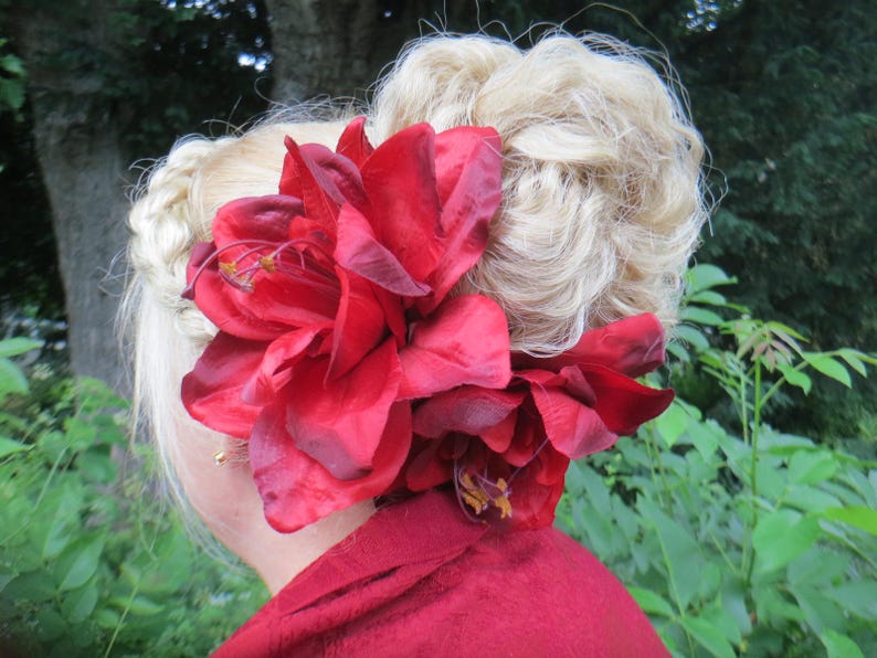 May include: A woman with blonde hair styled in a bun with a large red flower hair clip.