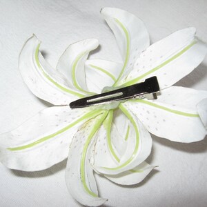 May include: White artificial lily flower with green veins and a silver hair clip attached.