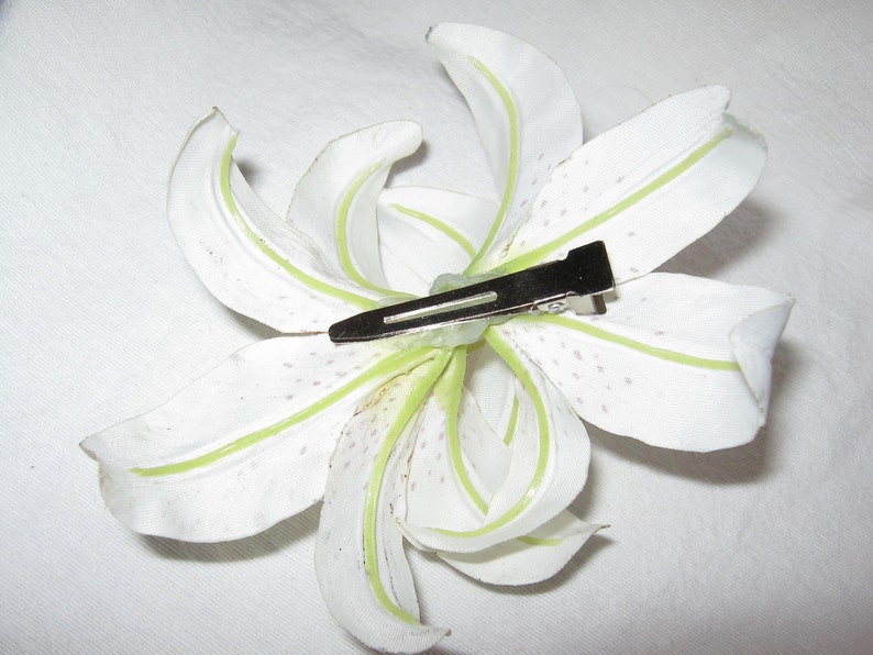 May include: White artificial lily flower with green veins and a silver hair clip attached.